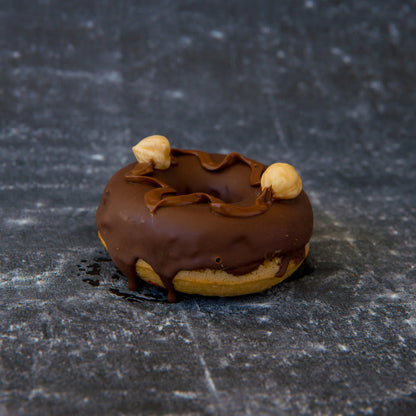 Chocolate-glazed FITbelly donut with nuts on a textured black surface