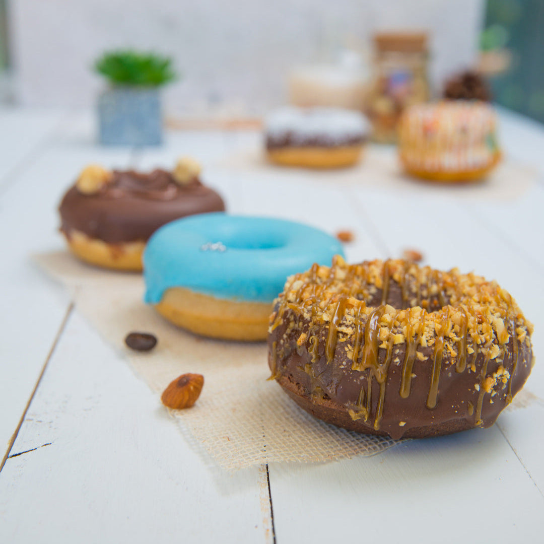 Assorted FITbelly donuts with different toppings on a light wooden surface.